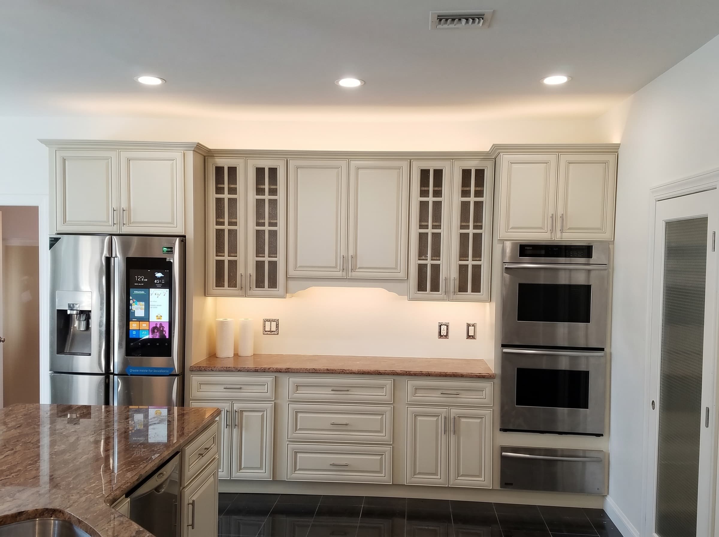 Kitchen with gray shaker cabinets, a large white island, brass pendant lights and wood flooring