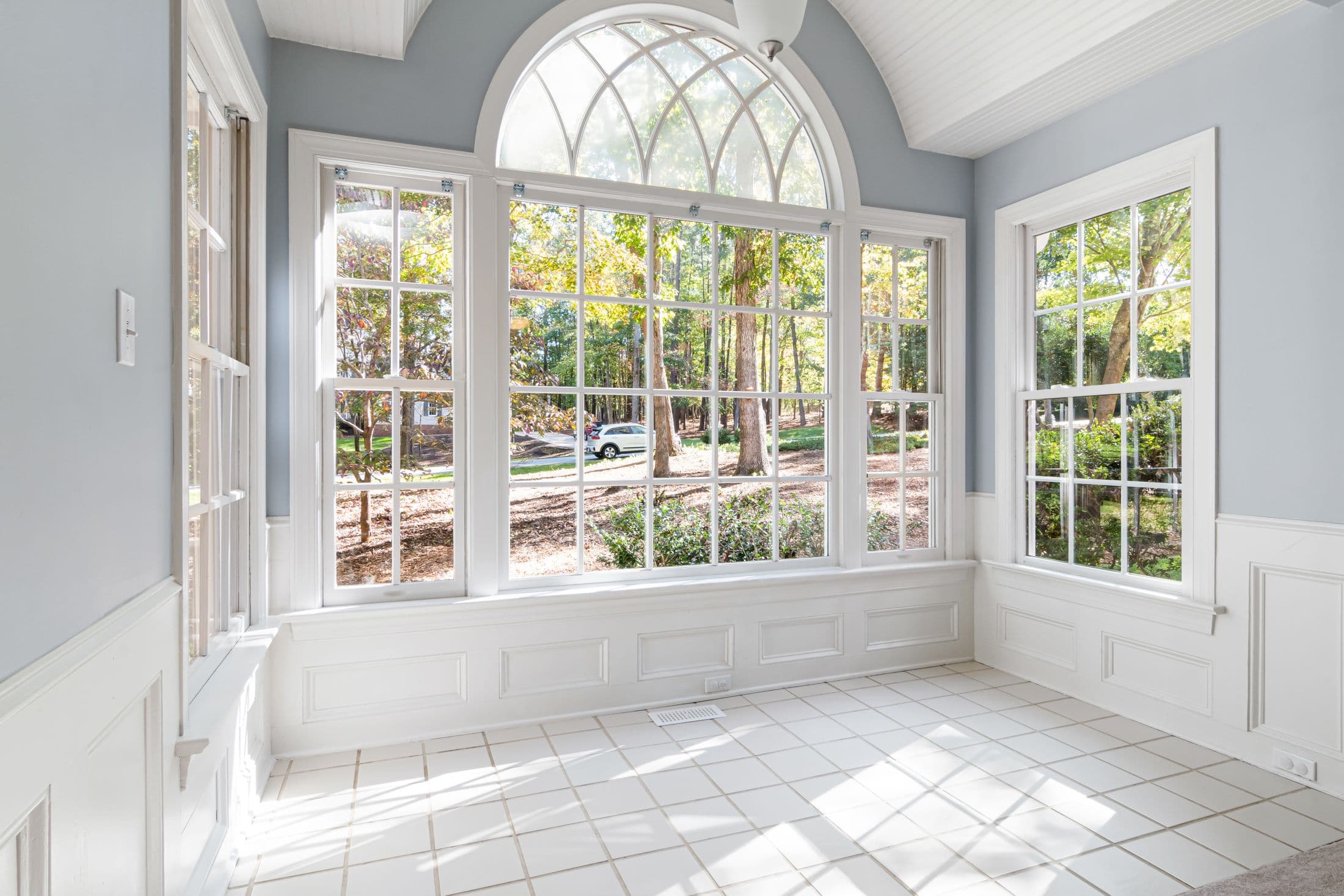 Home addition contractor near you: bright sunroom with an arched window, white trim and tiled floor