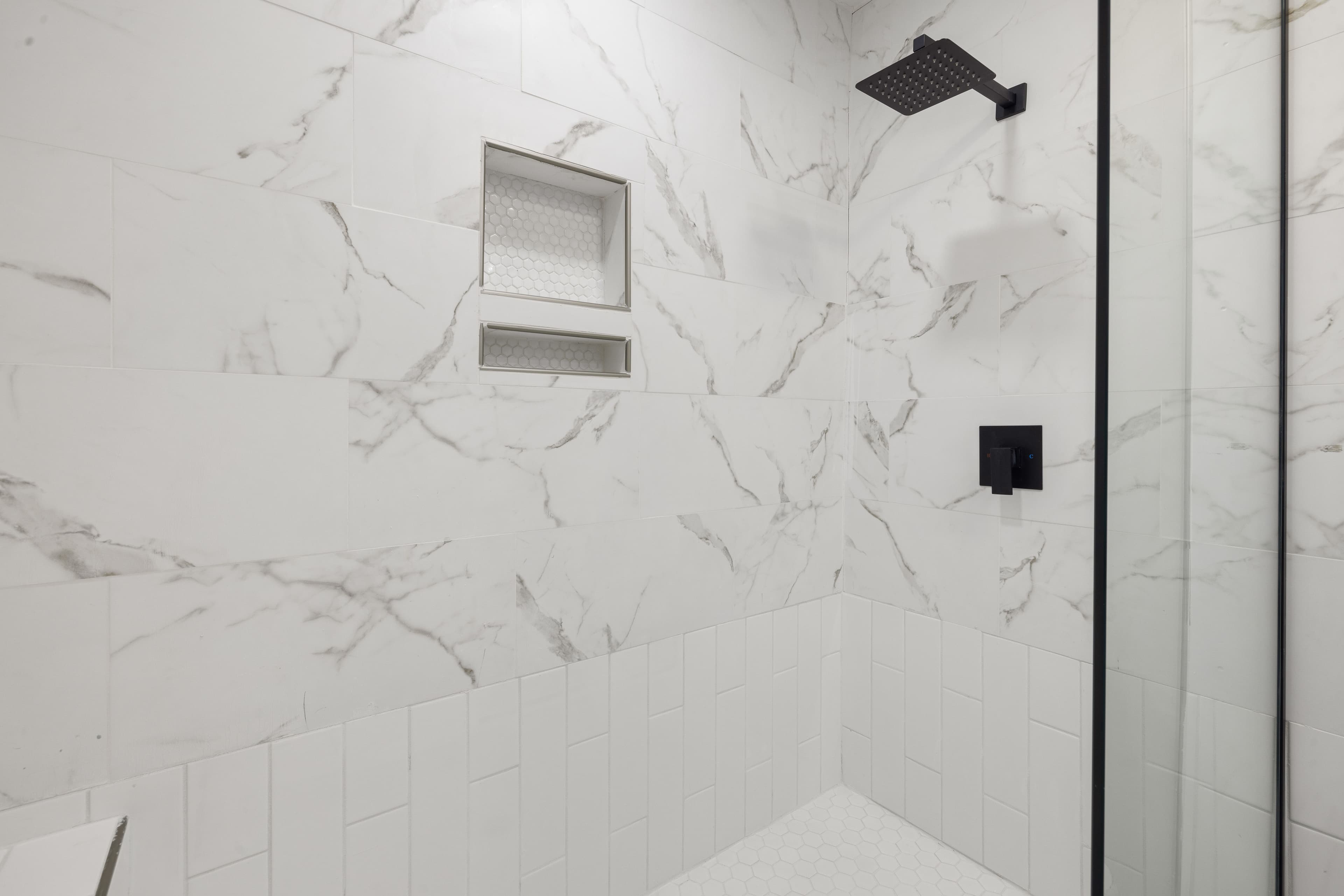 Tub to shower conversion near you: walk-in shower with marble-look tile, recessed shelves and black fixtures